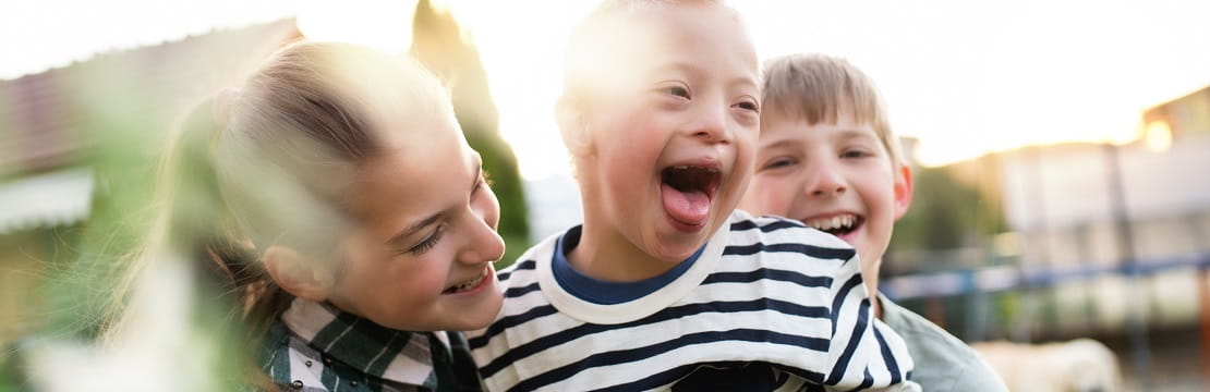 Child with Downs Syndrome plays with his two siblings in a backyard. 